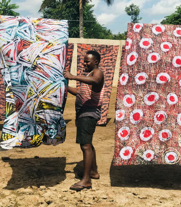 Person holding two large batim fabrics outdoors with trees in the background