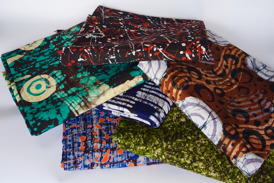 Stack of colorful batik fabric with various patterns on a white background from Uganda